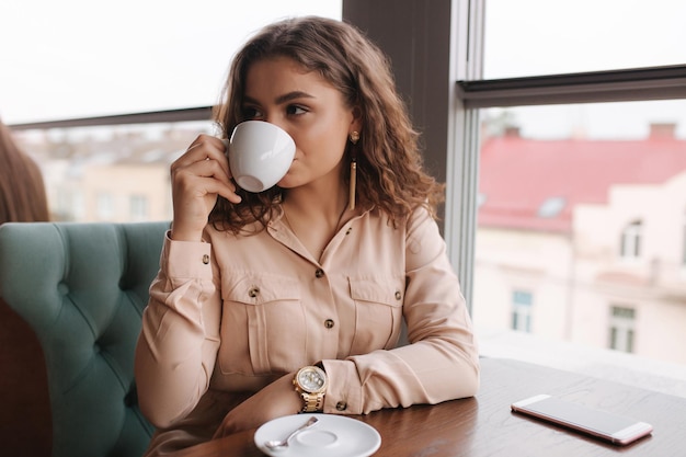 Young woman sitting in restaurant and drink cocktail Beautiful girl with curly hair smile to camera