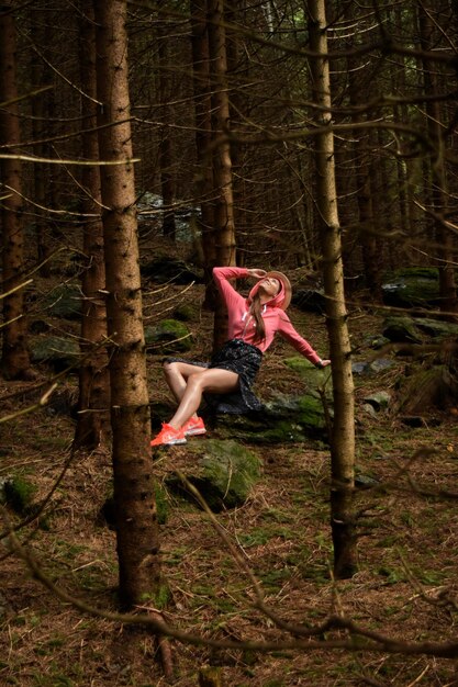 Photo young woman sitting on rock amidst trees in forest