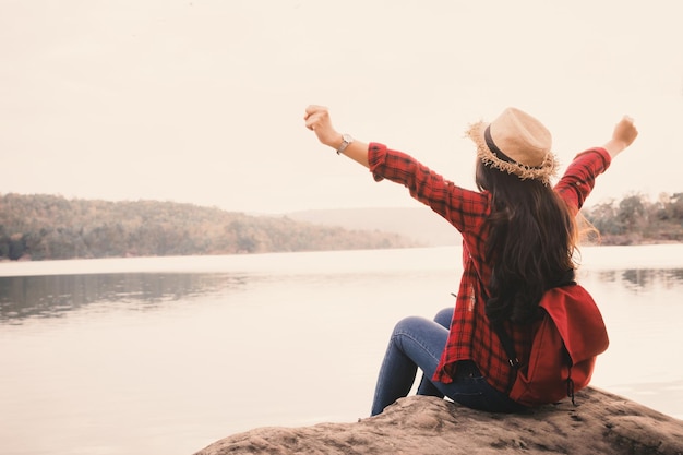 Foto giovane donna seduta su una roccia vicino al lago contro un cielo limpido