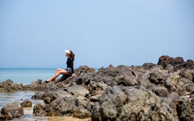 Молодая женщина сидит на скале у моря