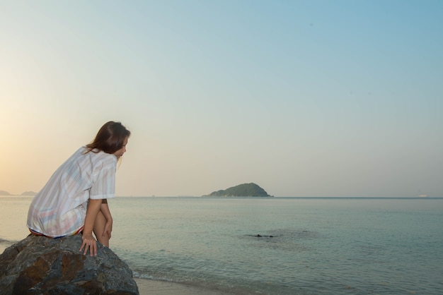 Молодая женщина, сидя на скале, наслаждаясь пляжем и морем