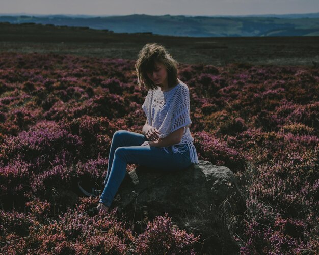 Photo young woman sitting on rock at field