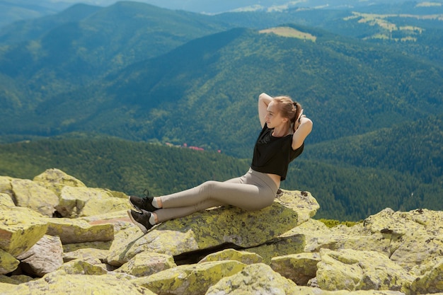 Молодая женщина сидит на скале и смотрит на горизонт.