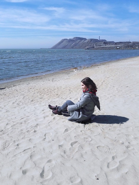 Photo young woman sitting on sand against sea at beach