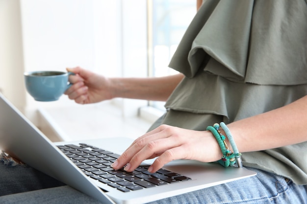 Young woman sitting on sill and using laptop at home