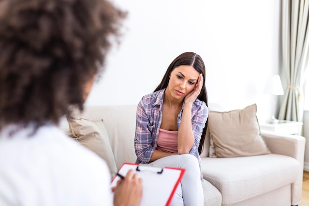 Young woman sitting on the sofa covering her face with hands feeling hopeless depressed or crying visiting psychotherapist finding out bad diagnosis or medical test results