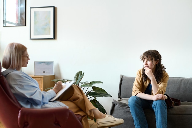 Young woman sitting on sofa and having psycho session with therapist in office