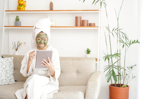 Young woman sitting on the sofa in the living room, she's using face mask and enjoying her day