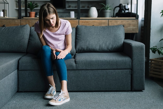 Photo young woman sitting on sofa suffering from knee pain