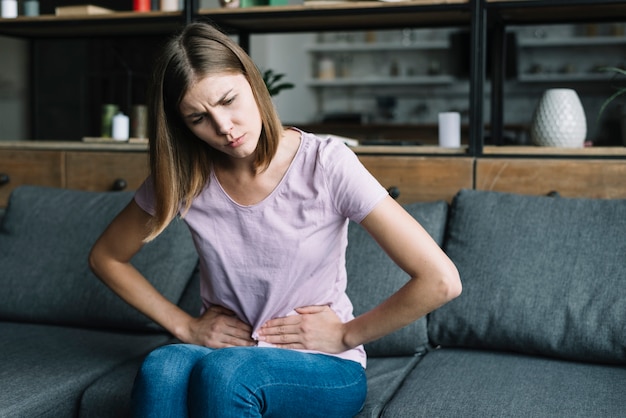 Foto giovane donna che si siede sul sofà che soffre dal dolore di stomaco