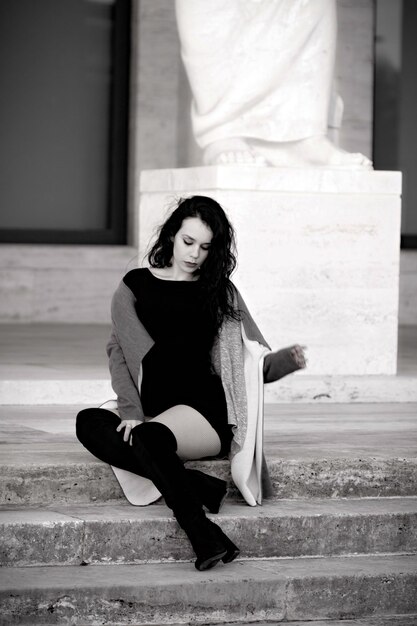 Young woman sitting on steps against statue in city