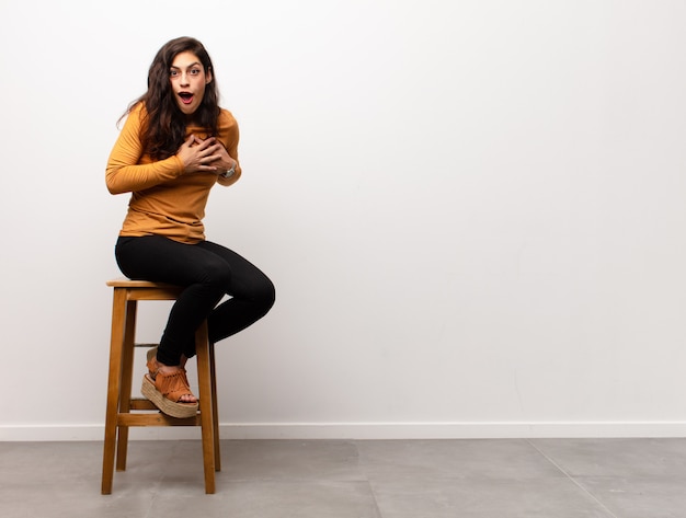 Young woman sitting on stool with surprised expression