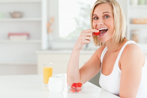 Young woman sitting at table eats strawberries