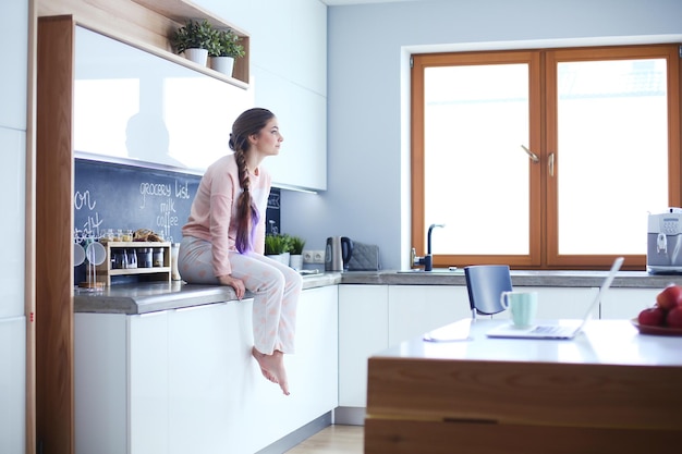 Photo young woman sitting on table in the kitchen