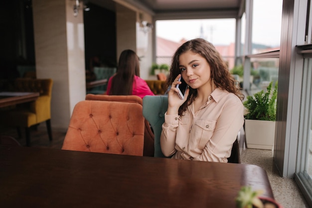 Young woman sitting on terrace and call to boyfriend Beautiful girl with curly hair Woman alone