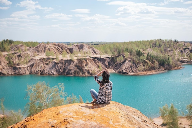 Giovane donna seduta in cima al montaggio e sentirsi libera e guardando il lago blu