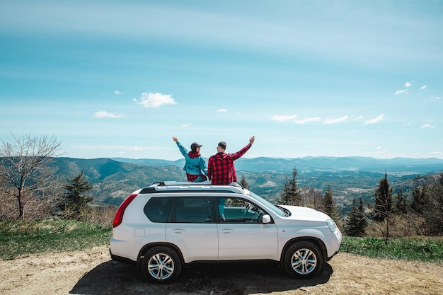 Young woman sitting on the top of the suv car at mountain peak enjoying the landscape view at summer sunny day