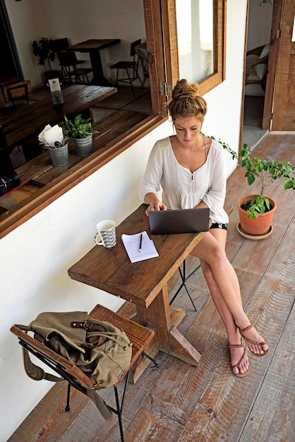 Young woman sitting on veranda of a coffee shop using laptop