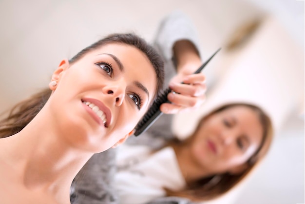 Молодая женщина сидит, пока парикмахер укладывает волосы