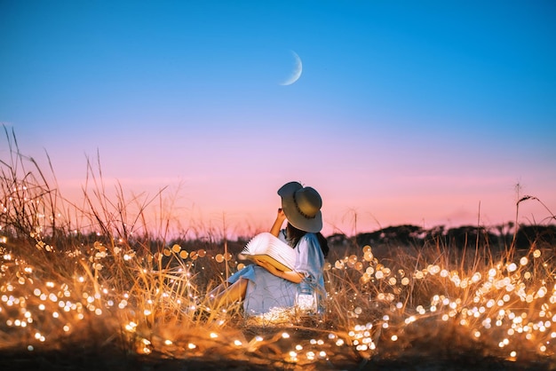 Foto giovane donna seduta con un libro in un campo illuminato contro il cielo