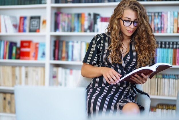 Photo young woman sitting with a book laptop in the library and taking learning notes concept of education