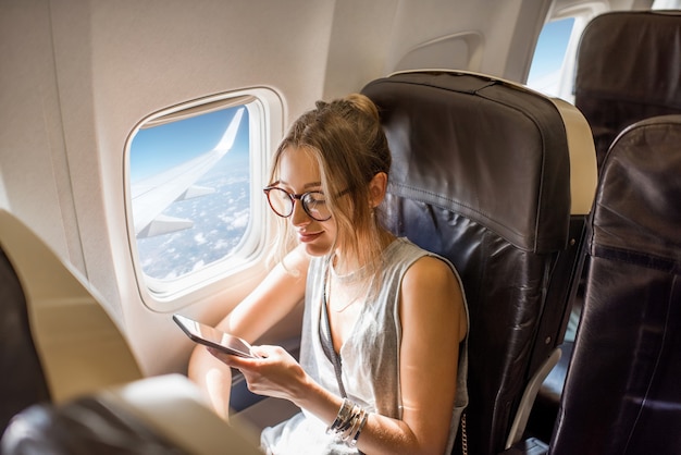 Photo young woman sitting with phone on the aircraft seat near the window during the flight in the airplane