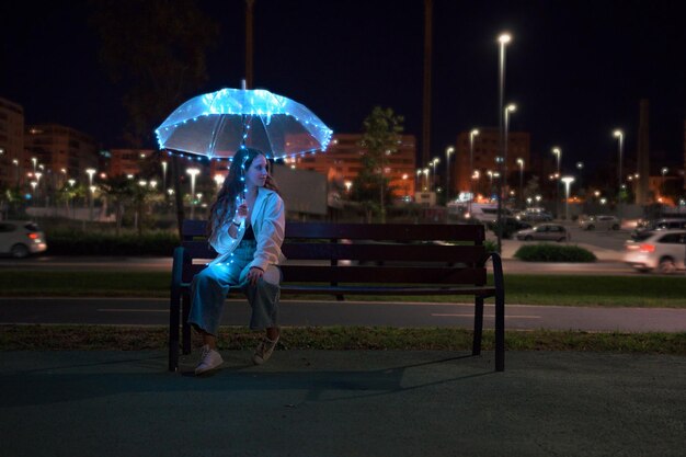밤에 조명이 있는 우산을 들고 앉아 있는 젊은 여성
