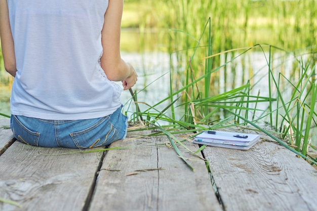 Young woman sitting on wooden pier, enjoying picturesque view of lake water