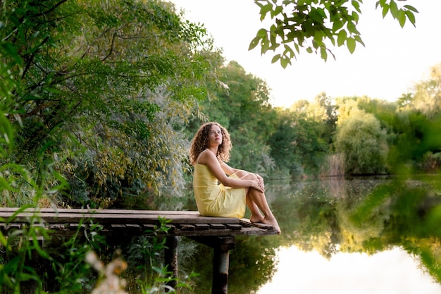 Foto giovane donna che si siede sul molo in legno vicino al lago