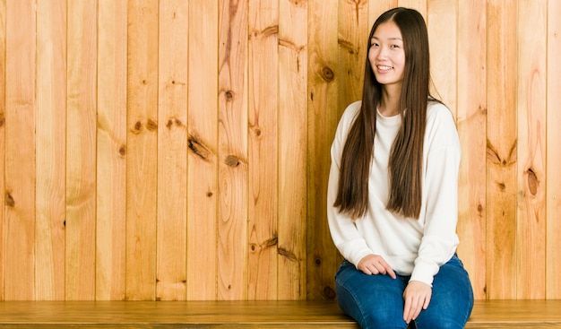 Young woman sitting on a wooden place looks aside smiling, cheerful and pleasant