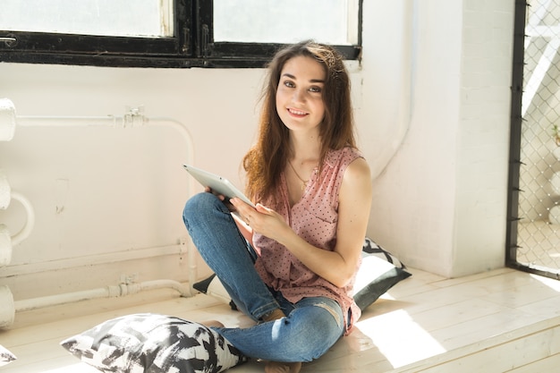 Young woman sitting on the wooden sill with tablet and pillows