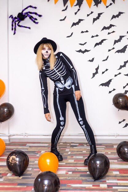 Foto giovane donna in un costume di scheletro su uno sfondo decorato con pipistrelli e un ragno in una festa di halloween