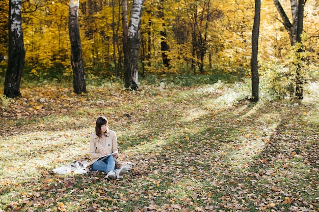 Young woman sketching near a lake in the autumn forest Sketching