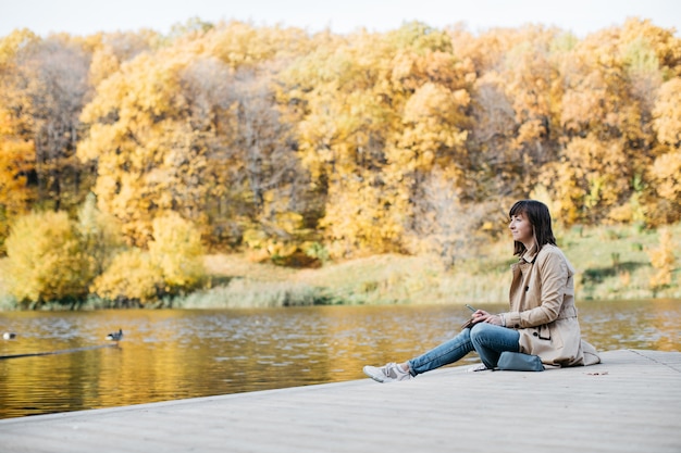 Photo young woman sketching near a lake in the autumn forest