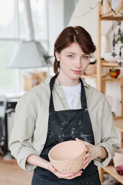 Young woman skilled in creating earthenware holding handmade clay bowl