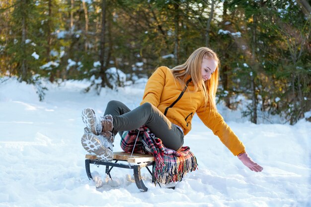 写真 若い女性が雪の森でスレッドを走る 黄色いジャケットを着た少女が 冬に松の木の中を散歩する