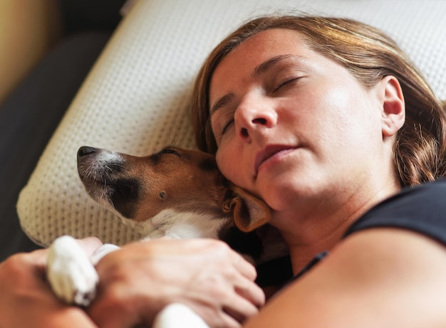 La giovane donna dorme con un piccolo cane, abbracciandola vicino, dettagli su teste e cuscino