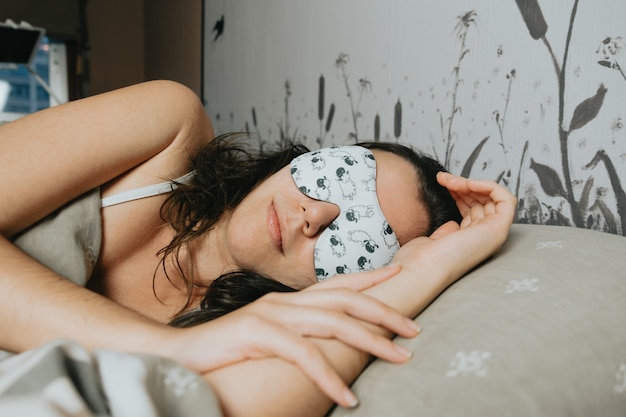 A young woman sleeping on the bed with a white sleeping mask