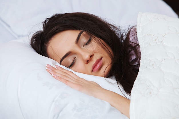 Young woman sleeping in sleepwear on the white linen in bed at home, top view.