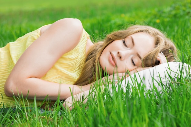 Foto giovane donna che dorme su un cuscino morbido nell'erba fresca di primavera