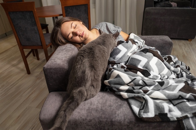 Молодая женщина спит со своей кошкой, британский кот гуляет с девушкой, пока она спит, кошка ползает под одеялом