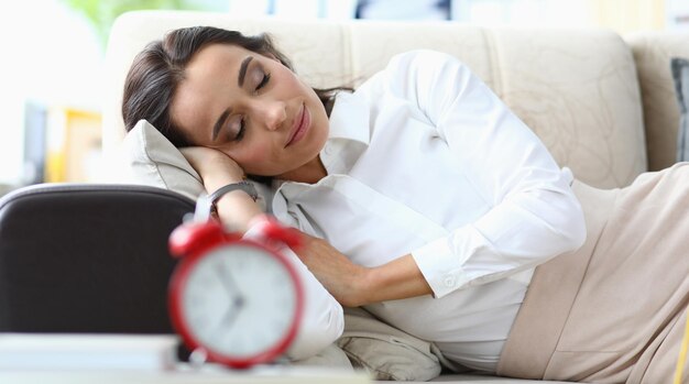 Young woman sleeps on sofa next to alarm clock