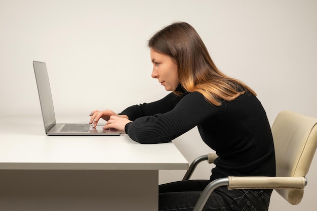 Giovane donna in posizione dinoccolata seduta nella stanza dell'ufficio, lavorando con il laptop