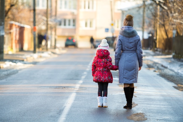 Young woman and small child daughter in warm clothing walking together