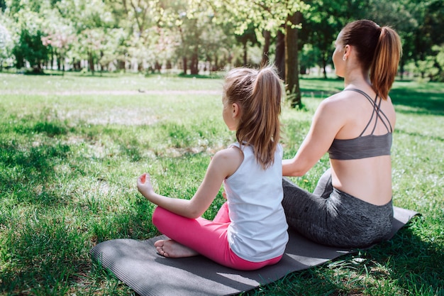 Young woman and small girl are sitting in lotus pose