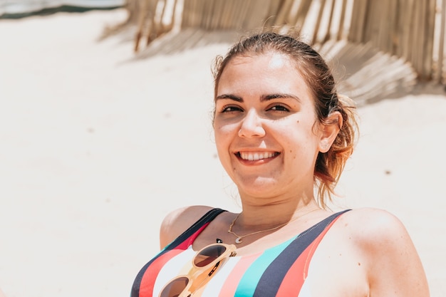 若い女性がビーチでカラフルな水着を着てカメラに微笑む、若い休日のコンセプト、コピースペース、ソーシャルネットワーク、サングラスのユーザーコンセプトを旅行する