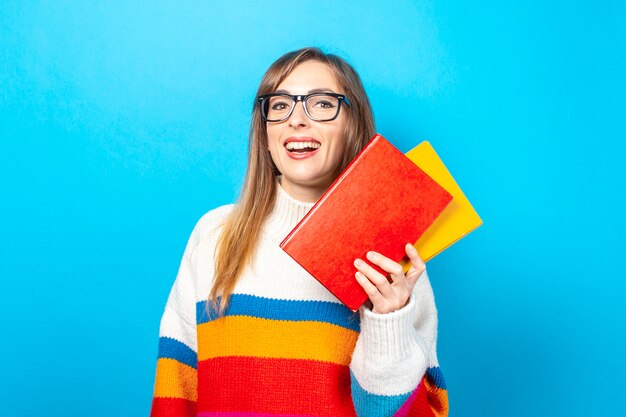 La giovane donna sorride e tiene i libri in sue mani su una priorità bassa blu