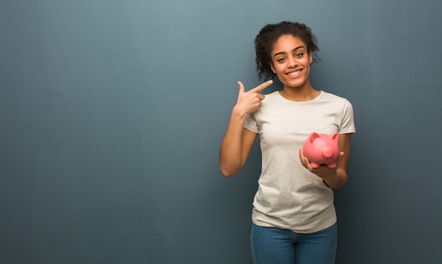 Young woman smiles, pointing mouth She is holding a piggy bank.