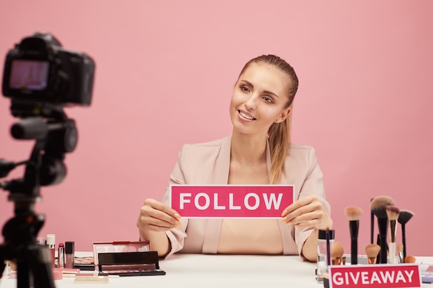 Young woman smiling at camera and says to her followers to follow her beauty blog