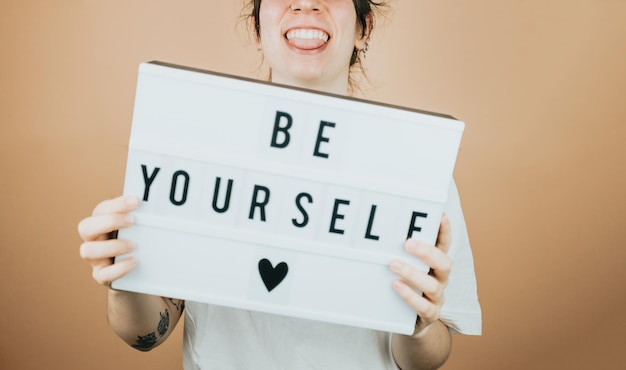Photo young woman smiling to camera while holding a sign be yourself with positive vibes to camera cheering people concepthelp and self help concept mental health color background with copy space